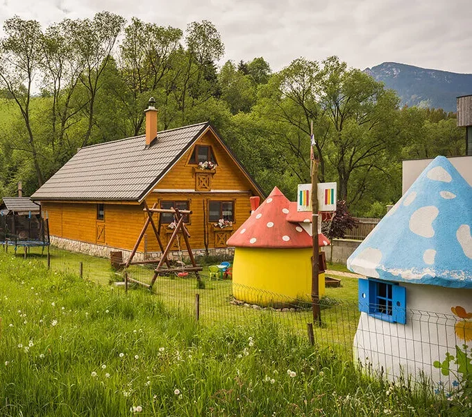 Drevená chatka s detskými hríbovými domčekmi a trampolínou na lúke